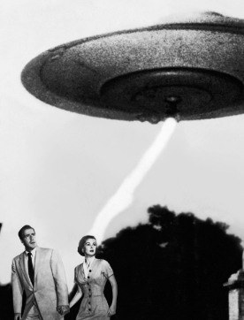 Two people standing below a UFO